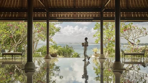 Hotel staff carrying flowers reflected onto floor of open-air pavilion 