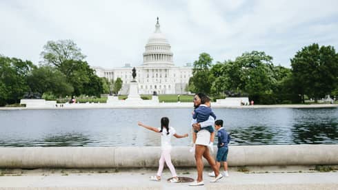 Woman and three children walk in front of the Capitol reflecting pool in Washington, DC, with Capitol building in background