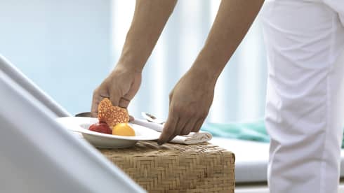 Close-up of hands placing white bowl with scoops of sorbet on wicker table