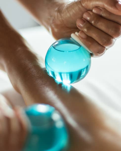 Close-up of a spa therapist performing a massage using blue glass cupping tools on a client’s leg.