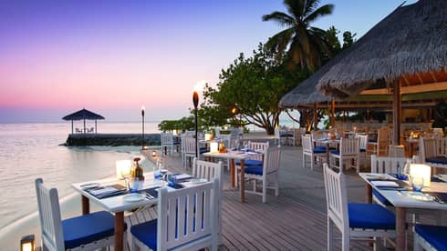 Reef Club on the water at sunset, with white tables on open patio and torches 