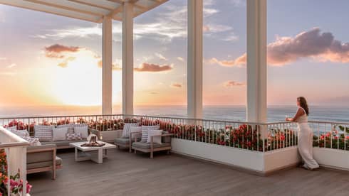 Woman gazes out to sunset view over the ocean from expansive terrace