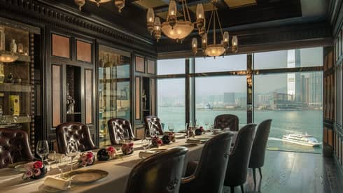 Long private dining table with roses under antique lamps by window overlooking harbour