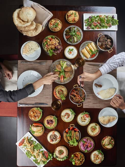 Aerial view of two people at dining table sharing hot and cold meze plates, Syrian and Lebanese meals