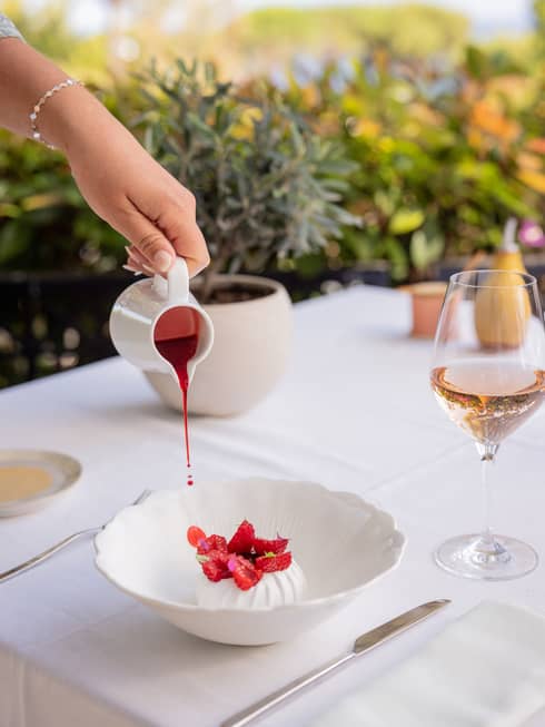 Round white dessert in a pool of raspberry sauce and topped with sliced raspberries in white bowl
