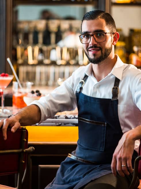 Portrait photo of Fifty Mils Head Mixologist Mica Rousseau sitting at bar