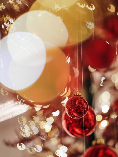 Close-up of red Christmas baubles hanging with blurred festive lights in the background