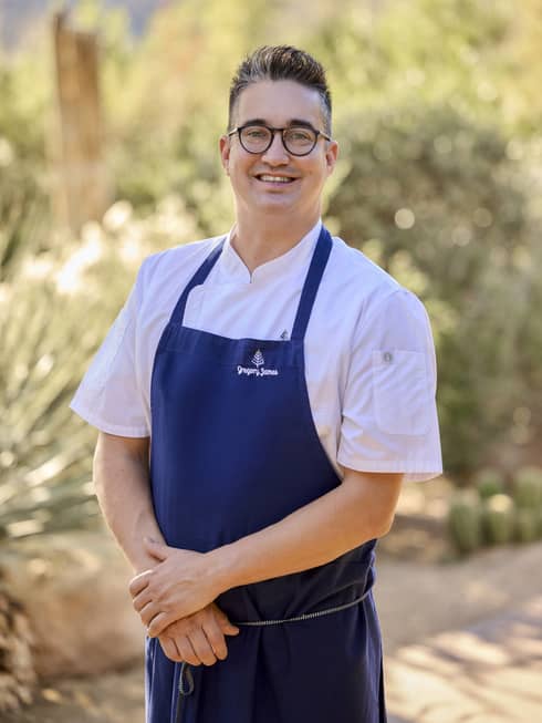 A chef poses wearing a blue apron.