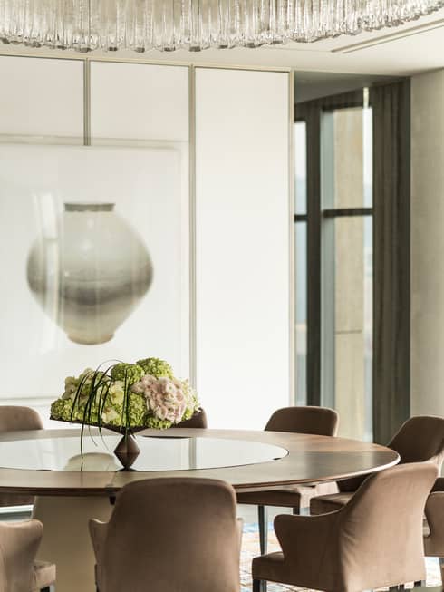 Floral display in vase on round table with upholstered chairs under modern, round crystal chandelier