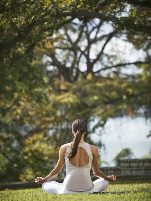 Back of woman meditating on sunny lawn