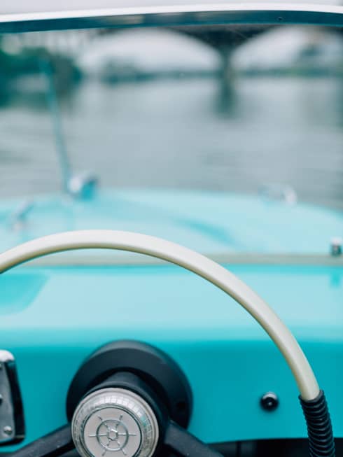 The steering wheel of an old boat with a bridge in the distance.