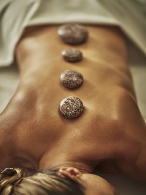 A woman lies on a spa table with four hot stones laid on her back