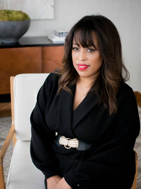 A woman in a black jacket sitting on a beige chair.