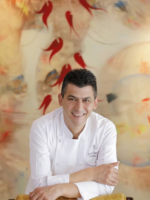 A portrait of Chef Savaş Aydemir leaning against a yellow chair