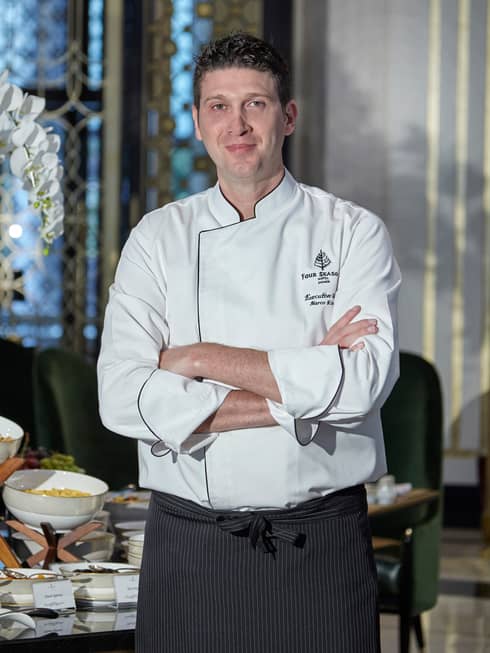 Portrait photo of Executive Chef Marco Riva with arms crossed, smiling, wearing white chef's coat