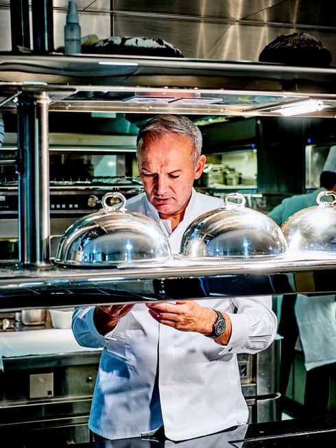 Le Cinq Chef Christian Le Squer behind kitchen line with metal cloche plate covers