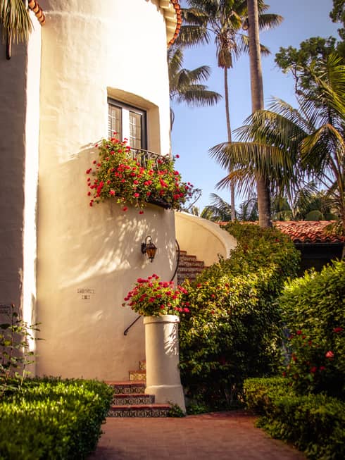 Curved staircase around white concrete building with window, flowers in planter, tropical garden