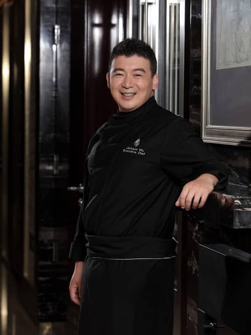 Portrait photo of Executive Chef Jackson Wu standing, smiling in black uniform
