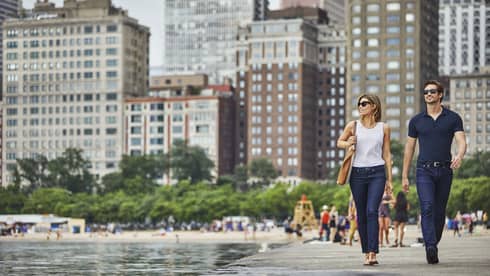 Man and woman wearing T-shirts, jeans and sunglasses stroll along Chicago waterfront