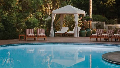 Striped pool chairs, white lounge chairs under white cabana curtains on swimming pool deck