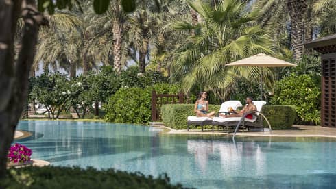 Two people in cabana chairs next to a pool. 
