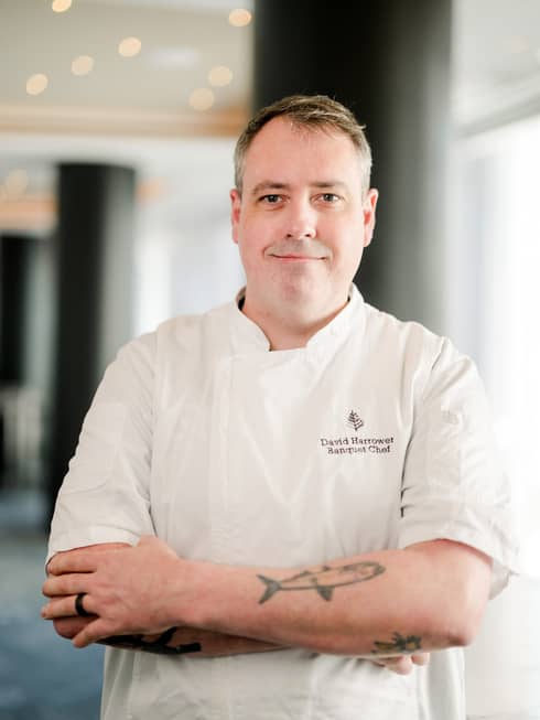 A chef in a white chefs coat standing in a well lit room.