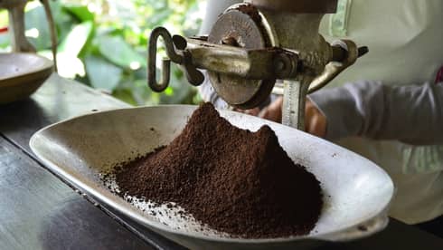 Large metal industrial-looking hand grinder with pile of ground Colombian coffee 