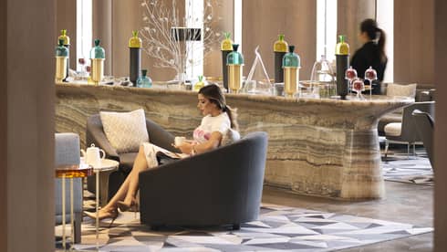 Woman drinks tea in large armchair by marble buffet bar