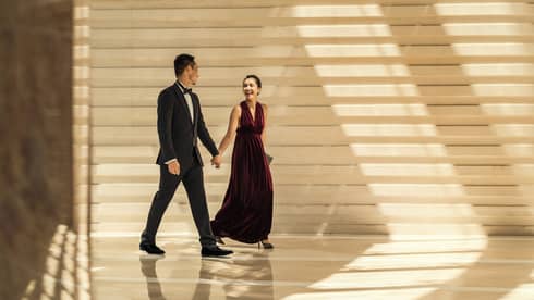 Man and woman in formal wear hold hands at Four Seasons Hotel Hong Kong.
