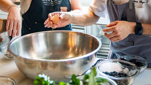 Two people stand in a kitchen prepping fresh ingredients to mix into a large silver bowl