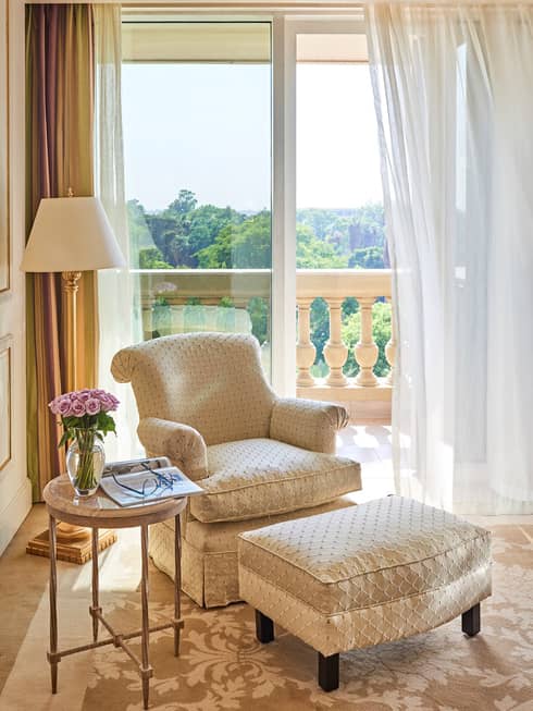 Beige and off white French-style chair with ottoman near window overlooking botanical gardens