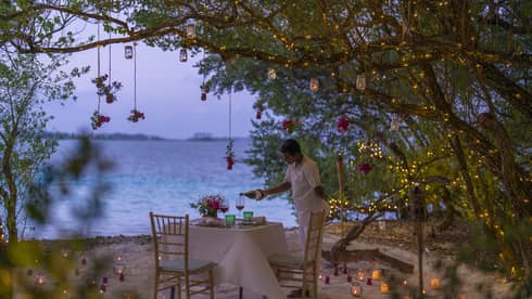 Resort staff pours wine into glass on beachside table set for two