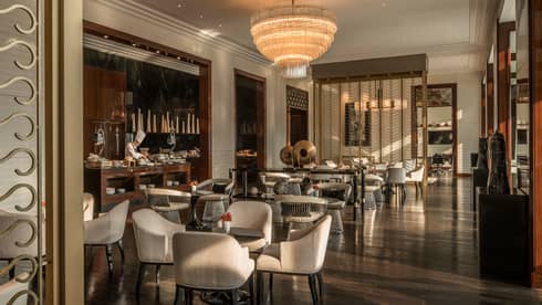 Executive Club lounge chef at bar by cocktail tables, chairs under tiered crystal chandelier