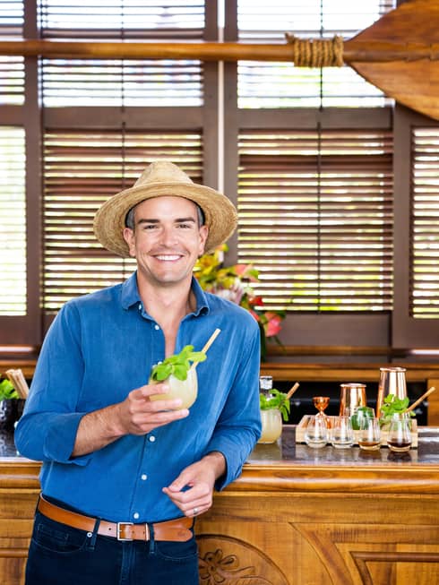 Man hearing straw hat holds a tropical drink at bar