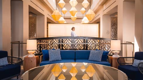 A woman walking behind a blue sofa in a lounge area with large geometric chandelier.