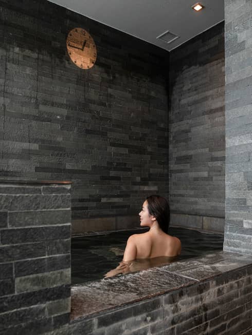Female guest soaks in the grey stone onsen bath