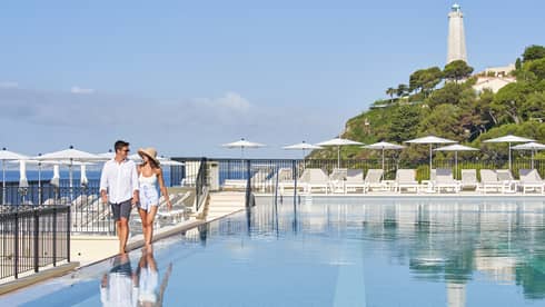 Couple walks along outdoor swimming pool deck at Club Dauphin