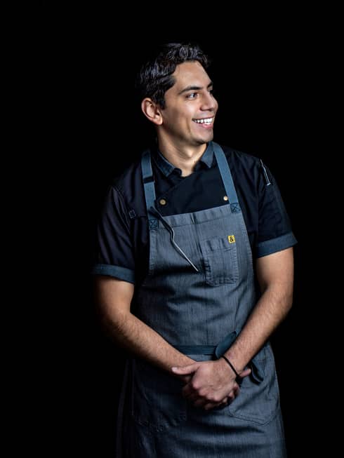 A chef in a dark grey apron on a black background.