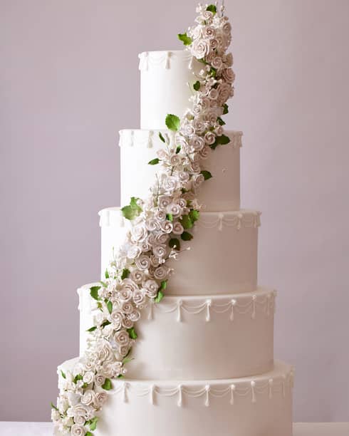 Five-tiered white wedding cake with a line of white-and-green fondant flowers rising diagonally from the bottom to the top