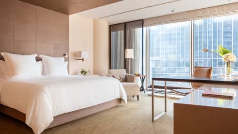 Guest room with large windows, city views, king bed, lamp, armchair and workspace