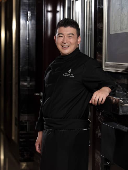 Portrait photo of Executive Chef Jackson Wu standing, smiling in black uniform