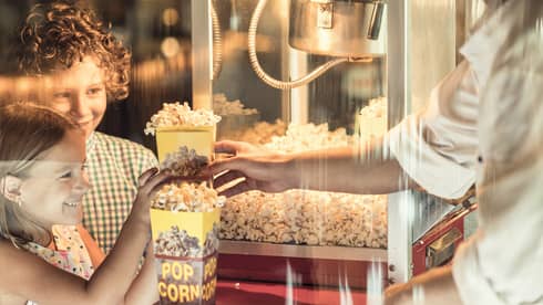 Two children smile as they wait to receive freshly popped popcorn from during BBK Brunch