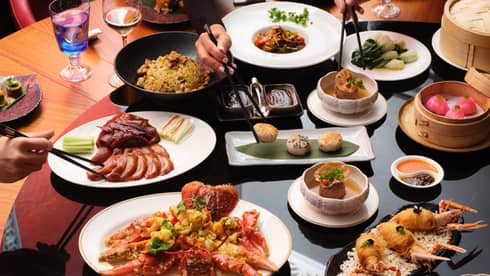 Round dining table with various dishes that people share, including meat and fried shellfish