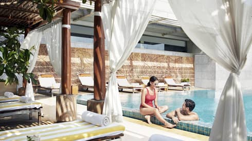 A couple lounges in the pool near a shaded cabana with fresh fruit