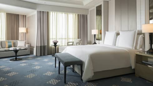 Spacious hotel room with blue pattern carpet, king sized bed and white bedding