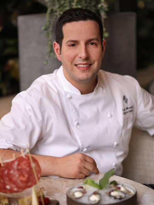 Portrait photo of Chef de Cuisine Luca Moriconi wearing white uniform at table