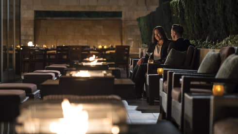 Two people in business attire sit in candle-lit cocktail lounge chairs with martinis