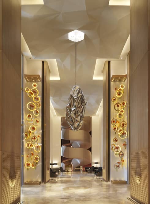 A paper mache installation that looks like a minimal bees hive hangs from the ceiling in a neutral lobby corridor 