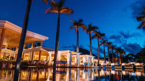 Under a twilight sky, the Resort’s lights reflect on the surface of a dark pool lined by palm trees and cloth-covered tables.