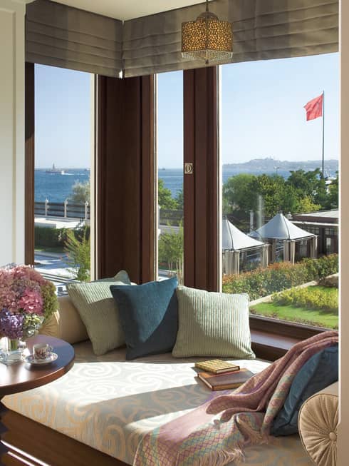Cushioned bench with pillows, table in front of large bay window overlooking patio